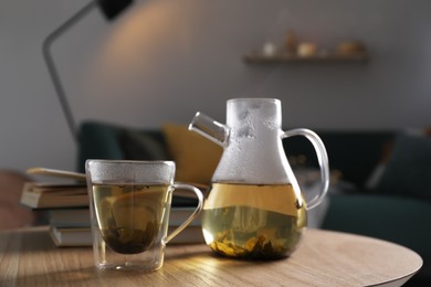 Photo of Glass teapot and cup of hot tea on wooden table in living room. Cozy home atmosphere