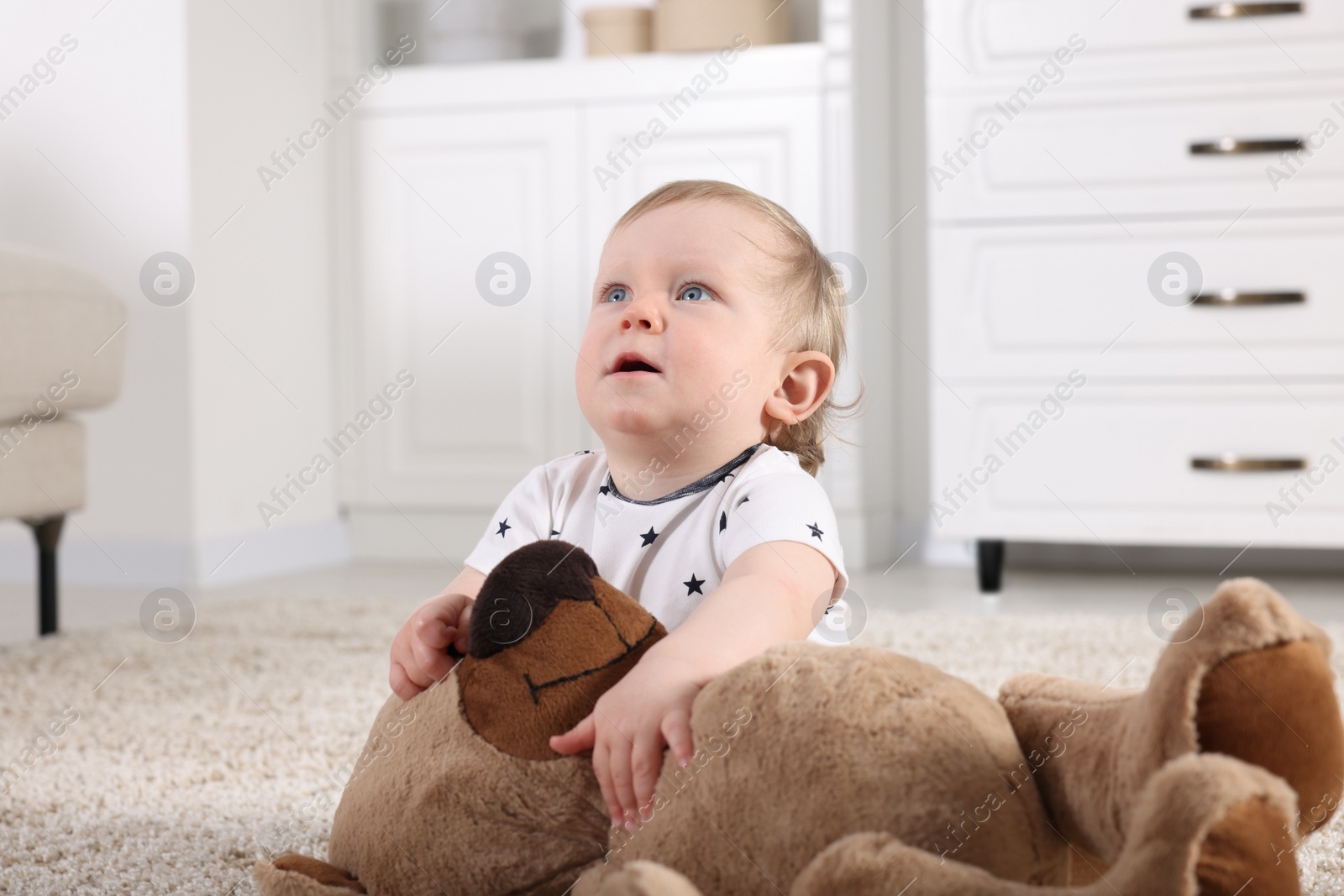 Photo of Cute little child with teddy bear on carpet at home