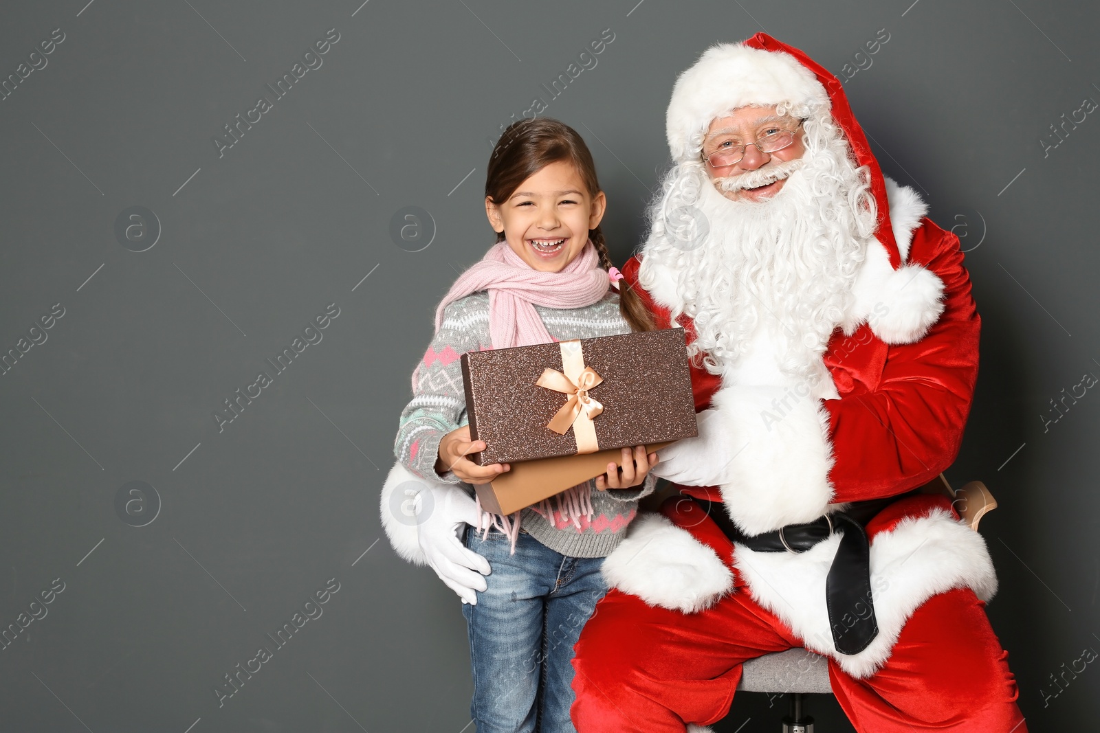 Photo of Little girl with gift box and authentic Santa Claus on grey background