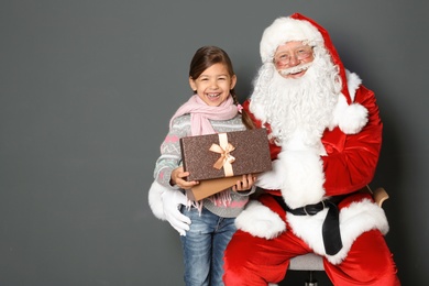 Little girl with gift box and authentic Santa Claus on grey background