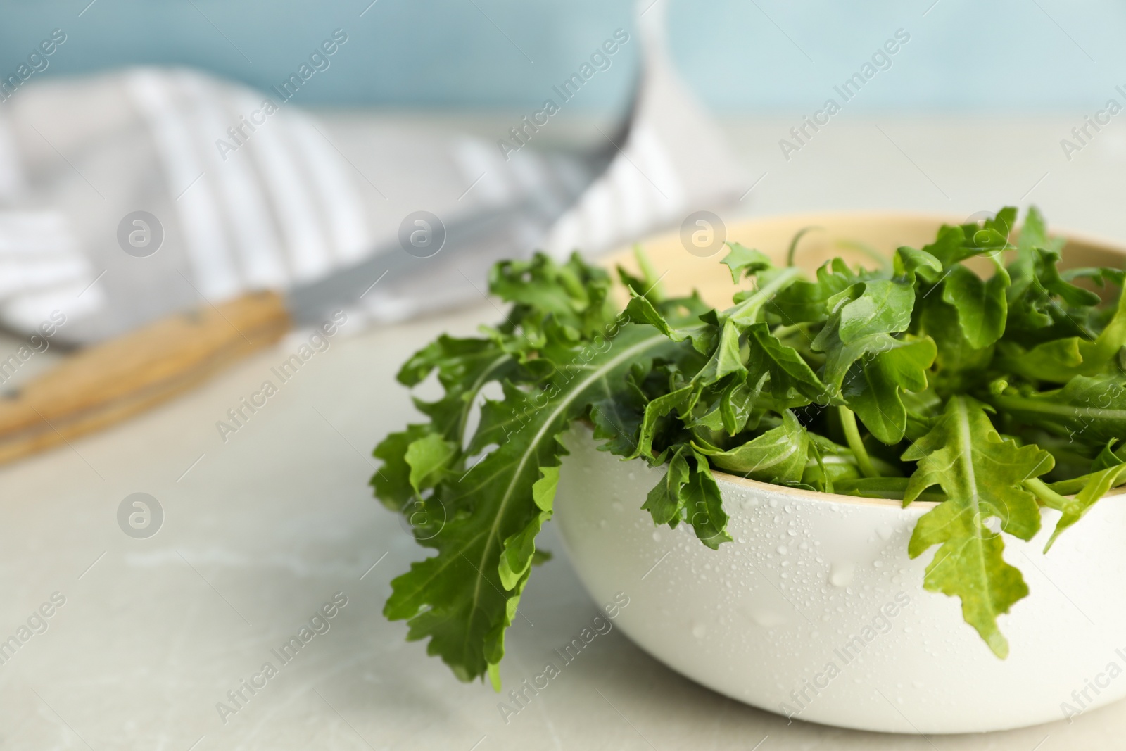 Photo of Fresh arugula in bowl on light grey table. Space for text