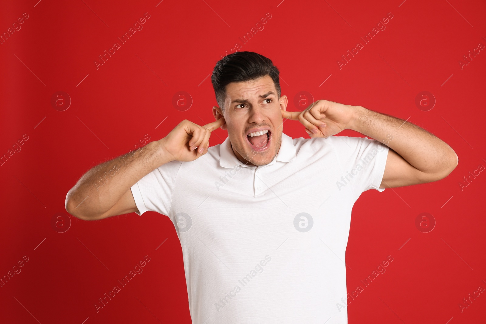 Photo of Emotional man covering ears with fingers on red background