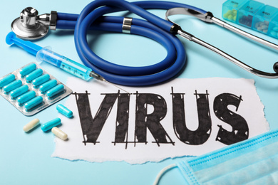 Photo of Word VIRUS, stethoscope and medicines on light blue background, closeup