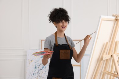 Photo of Young woman painting on easel with canvas in studio