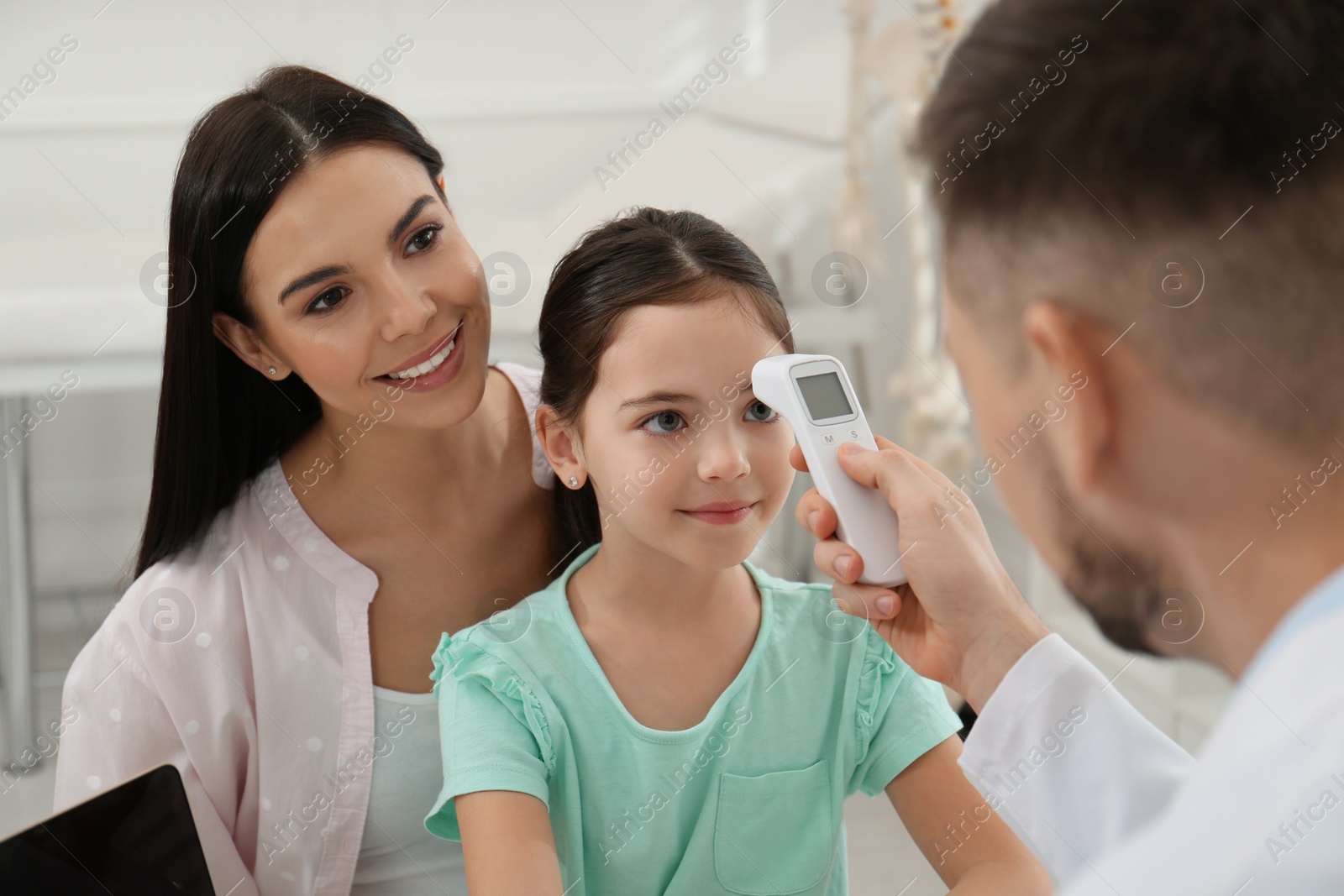 Photo of Mother with daughter visiting pediatrician in hospital. Doctor measuring little girl's temperature