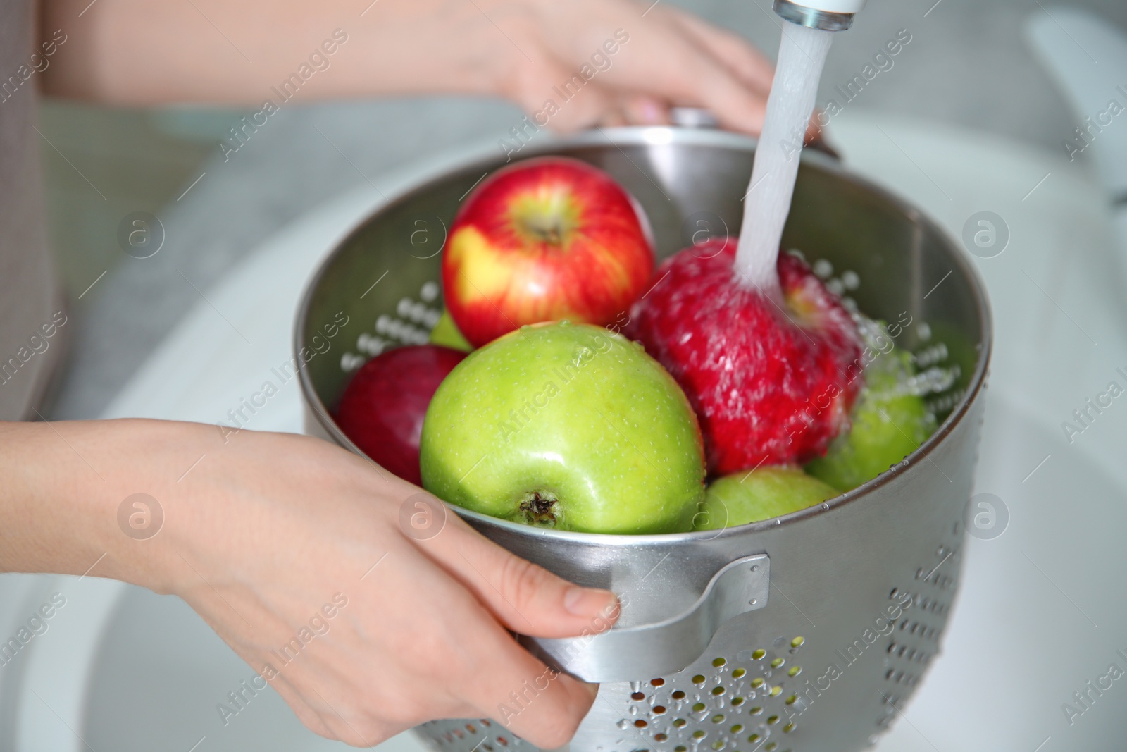 Photo of Young woman washing ripe apples in kitchen