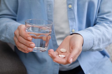 Photo of Woman with glass of water and pills on sofa, closeup