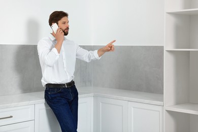 Photo of Man talking on smartphone in empty kitchen