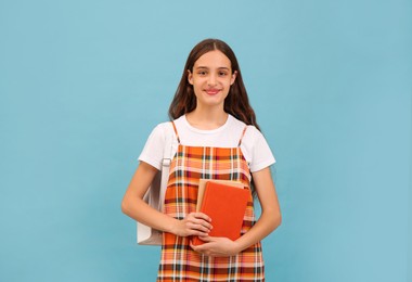 Photo of Teenage student with backpack and books on light blue background