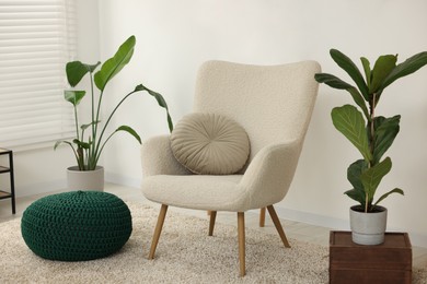 Photo of Comfortable armchair, pouf and houseplants in living room. Interior design