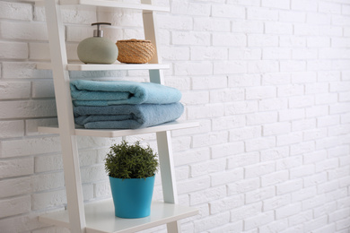 Photo of Clean soft towels and soap dispenser on shelves near white brick wall. Space for text