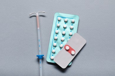 Photo of Birth control pills and intrauterine device on light grey background, flat lay. Choosing method of contraception