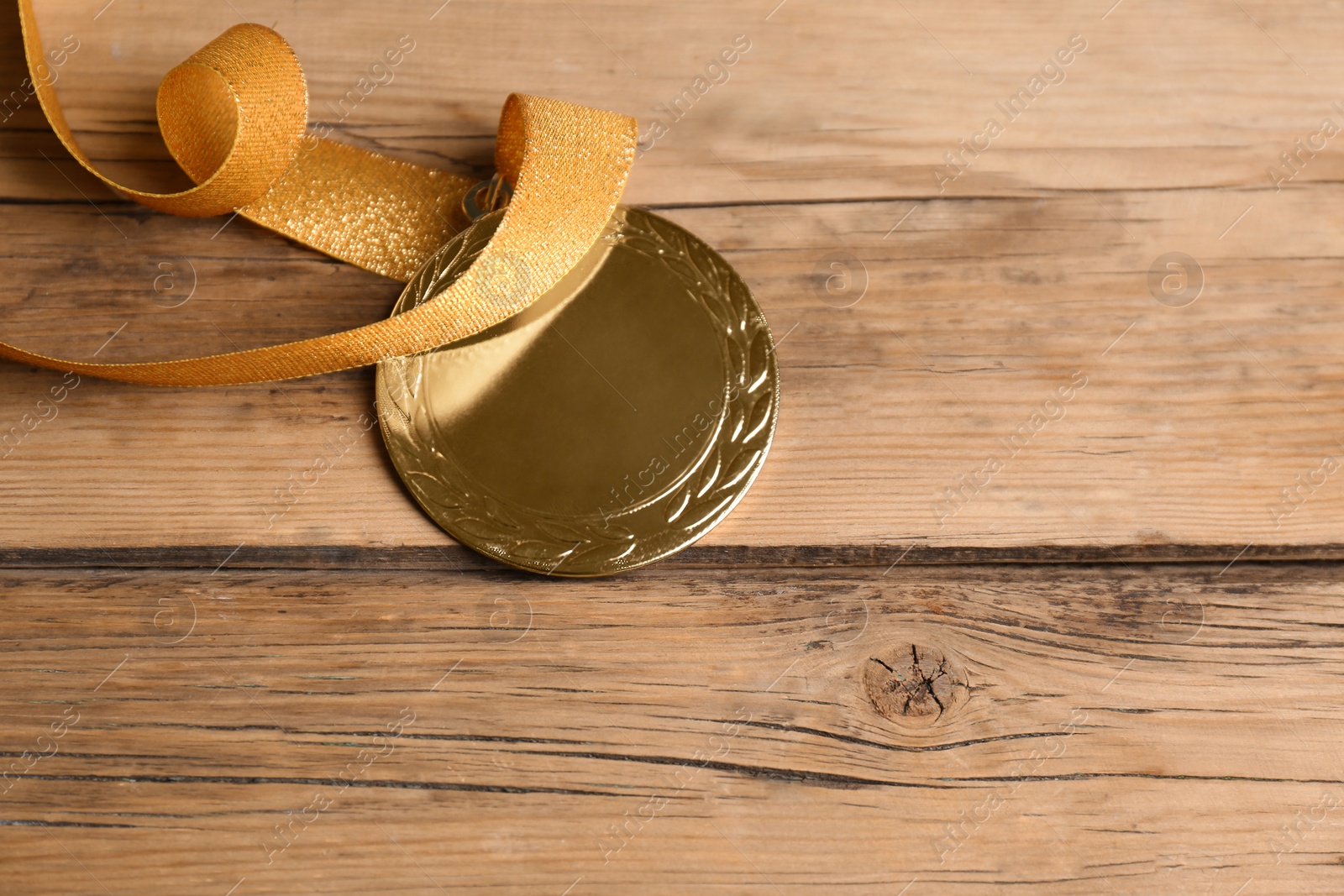 Photo of Gold medal with yellow ribbon on wooden background, closeup. Space for design