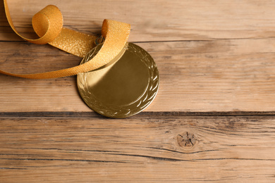 Photo of Gold medal with yellow ribbon on wooden background, closeup. Space for design