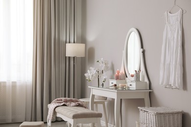 Photo of Wooden dressing table with decorative elements and makeup products in room. Interior design