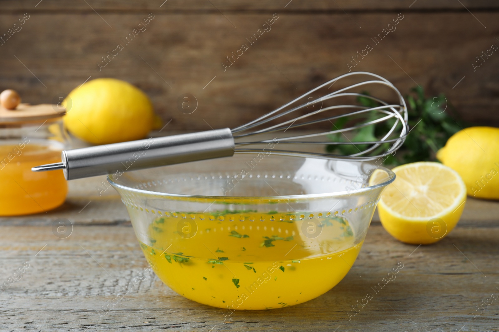 Photo of Whisk and bowl with lemon sauce on wooden table. Delicious salad dressing