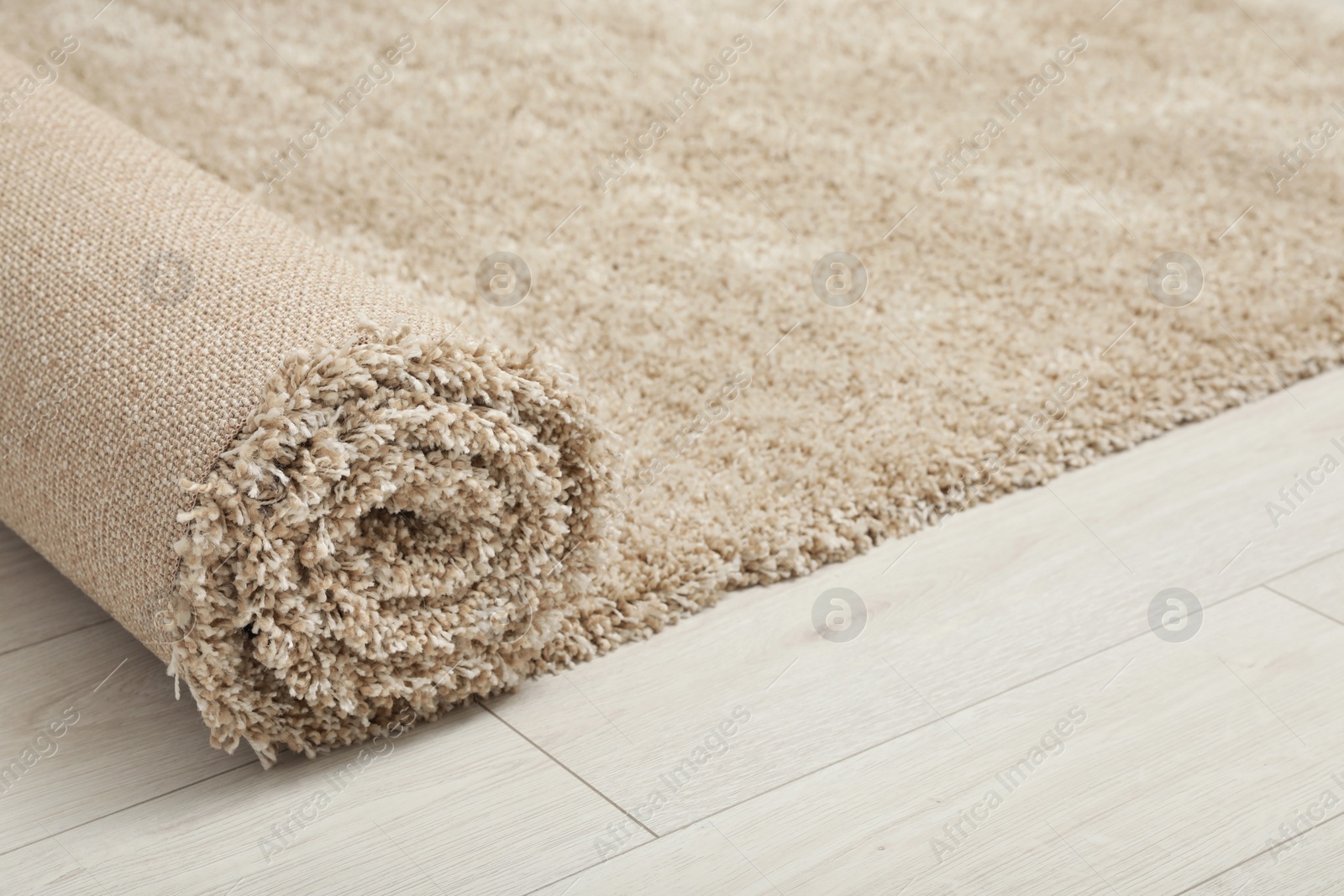 Photo of Rolled beige carpet on floor, closeup. Space for text