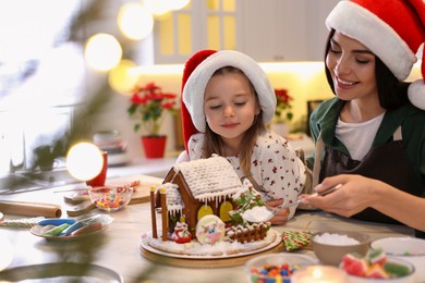 Photo of Mother and daughter decorating gingerbread house at table indoors