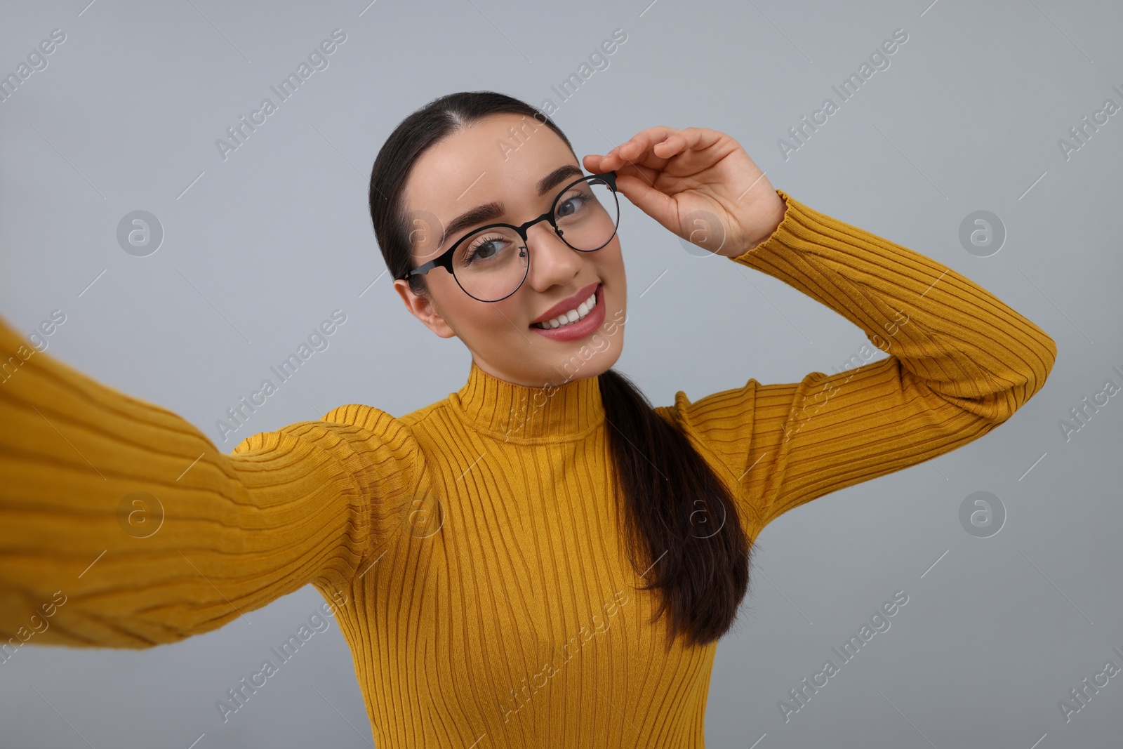 Photo of Smiling young woman taking selfie on grey background