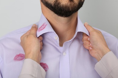 Woman noticed lipstick kiss marks while straightening her husband's shirt against white background, closeup