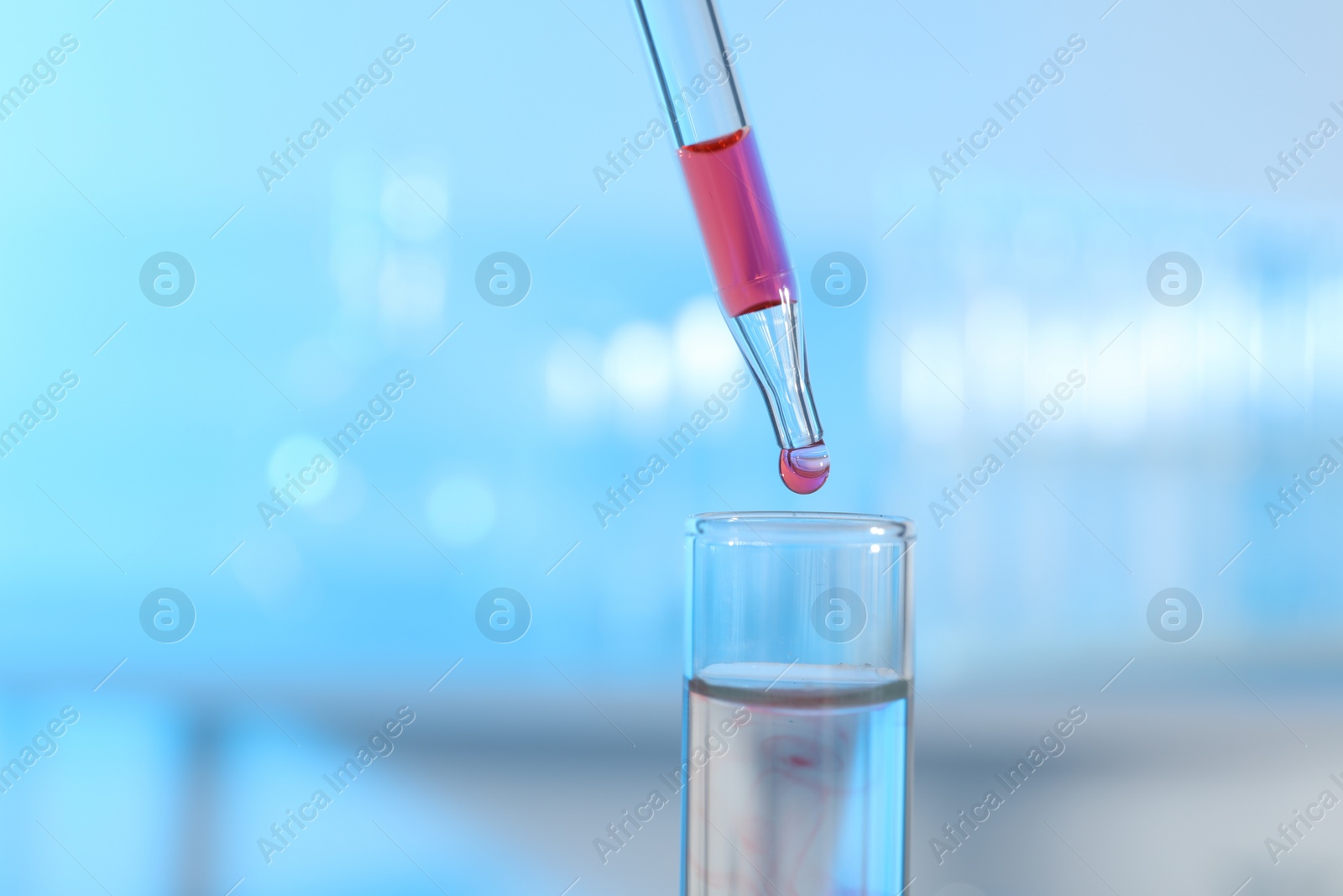 Photo of Dripping liquid from pipette into test tube on light background, closeup