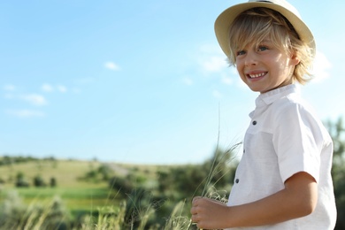 Cute little boy wearing stylish hat outdoors, space for text. Child spending time in nature