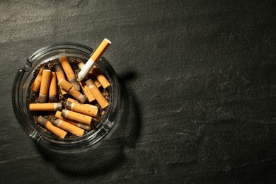 Photo of Glass ashtray with cigarette stubs on dark grey table, top view. Space for text