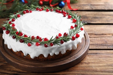 Traditional Christmas cake decorated with rosemary and cranberries on wooden table, closeup