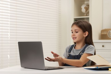 Photo of Cute girl having online lesson at white table indoors