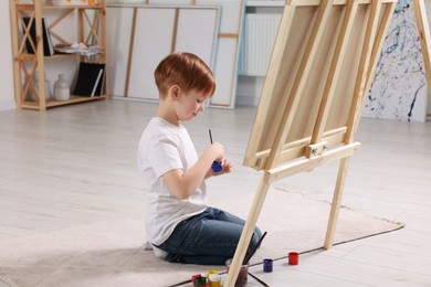 Little boy painting in studio. Using easel to hold canvas