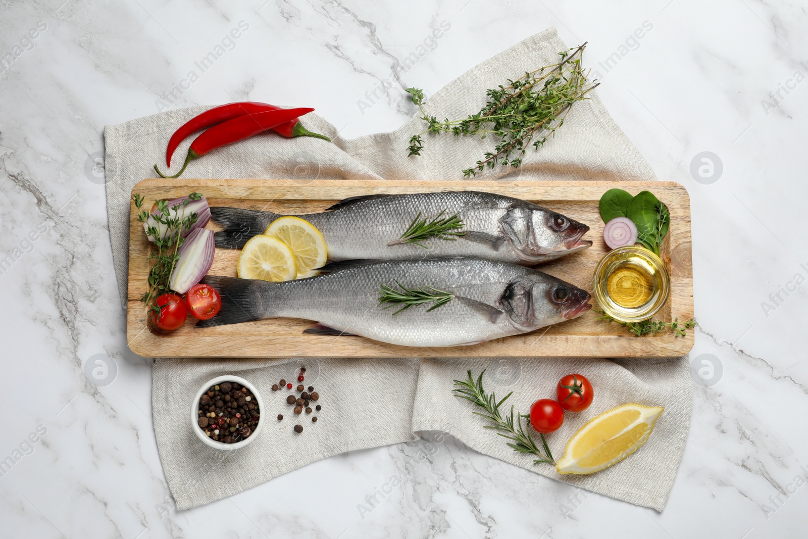 Photo of Tasty sea bass fish and ingredients on white marble table, flat lay