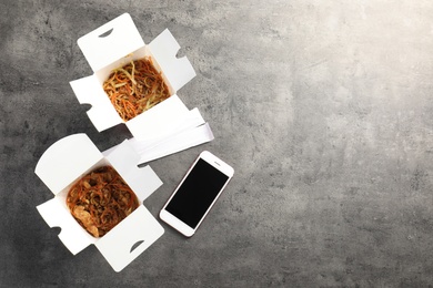 Photo of Smartphone with space for text and Chinese noodles on grey table, top view. Food delivery