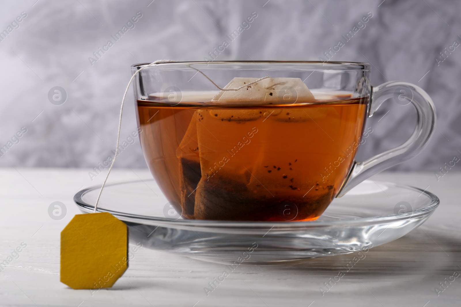 Photo of Tea bag in glass cup on white wooden table, closeup