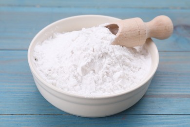 Bowl and scoop of natural starch on light blue wooden table, closeup