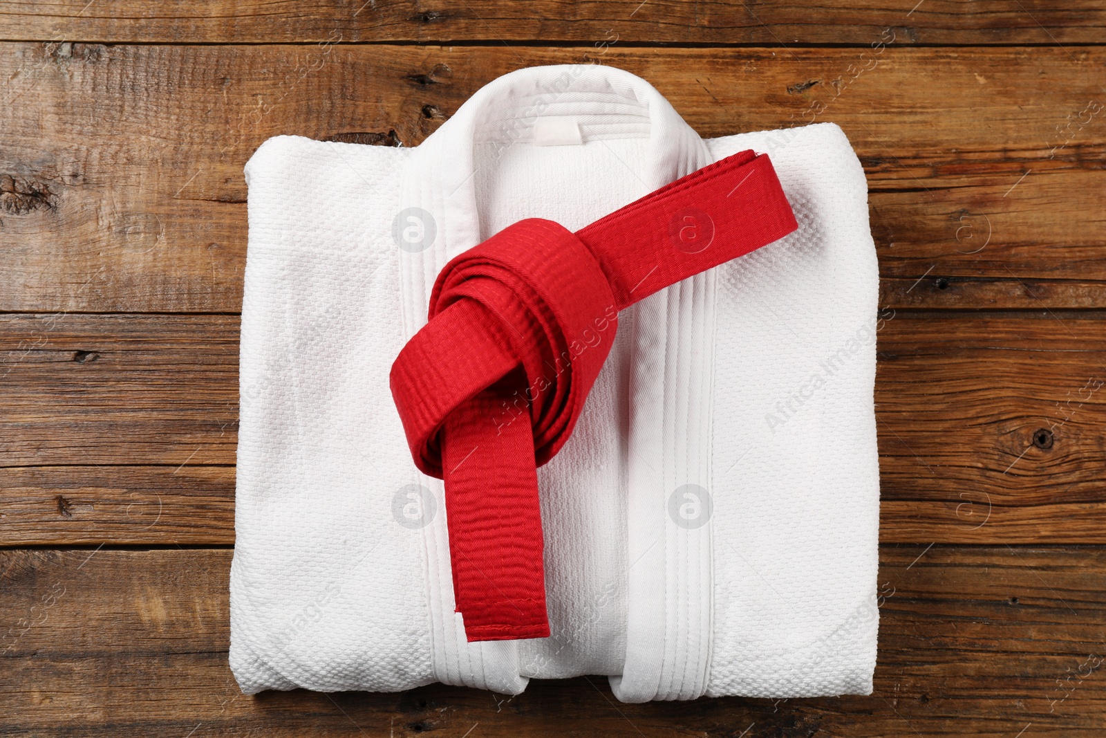 Photo of Red karate belt and white kimono on wooden background, top view