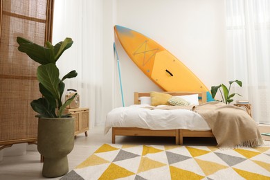 Photo of Large comfortable bed, SUP board and green houseplants in stylish bedroom. Interior design