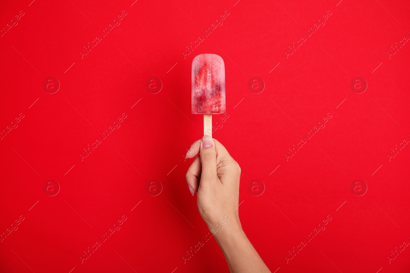 Photo of Woman holding berry popsicle on red background, closeup