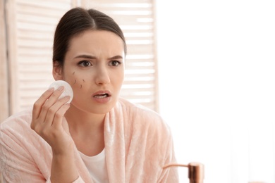 Beautiful woman with fallen eyelashes holding cotton pad indoors