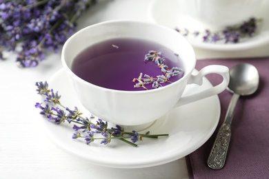 Photo of Fresh delicious tea with lavender and beautiful flowers on white wooden table, closeup
