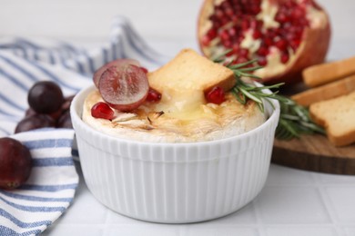Photo of Tasty baked camembert with crouton, grape and rosemary on white tiled table, closeup