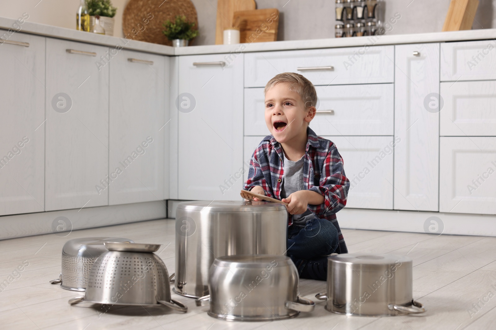 Photo of Little boy pretending to play drums on pots in kitchen