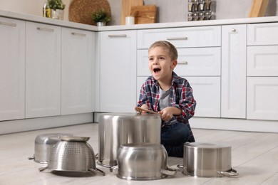 Little boy pretending to play drums on pots in kitchen
