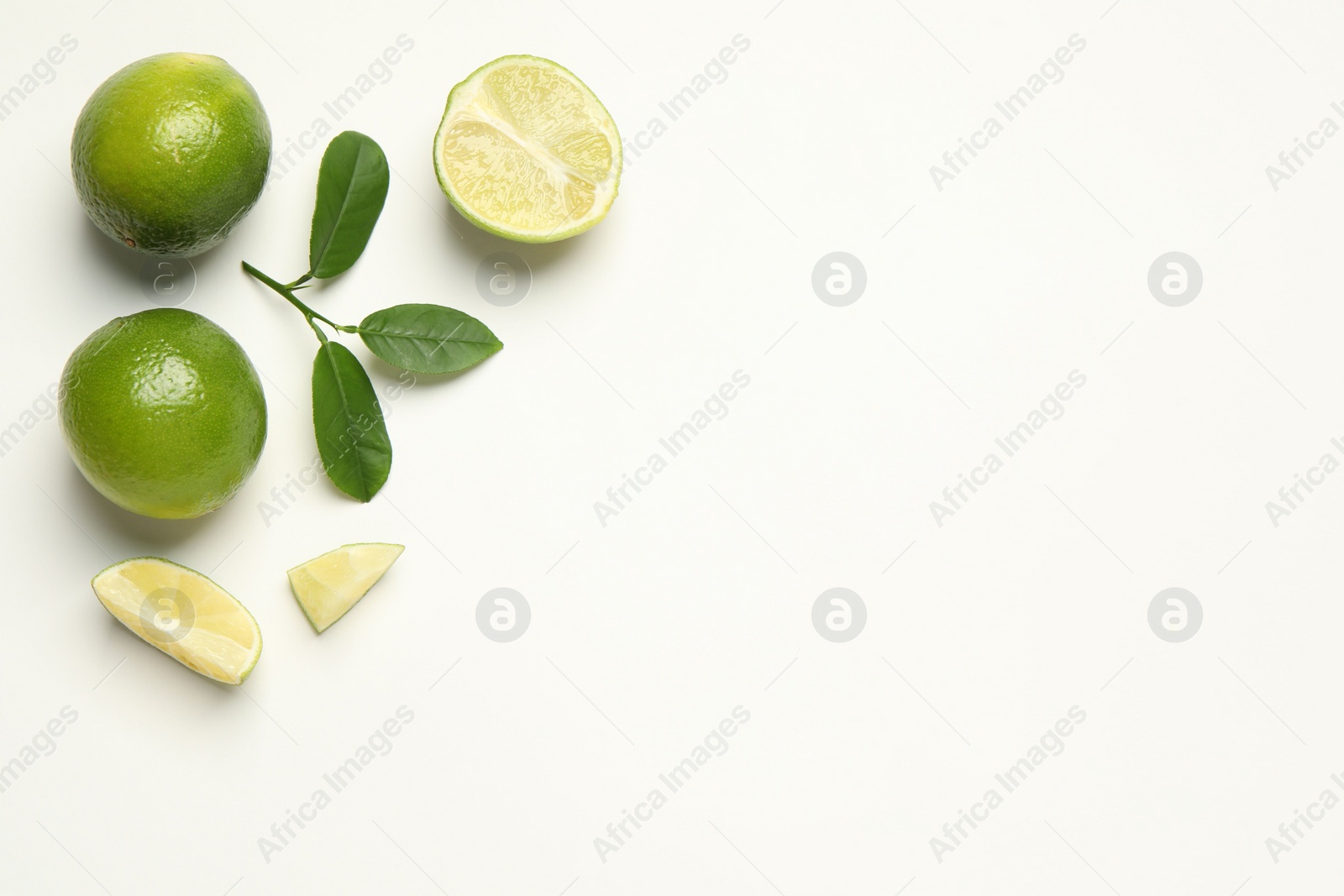 Photo of Whole and cut fresh ripe limes with green leaves on white background, flat lay