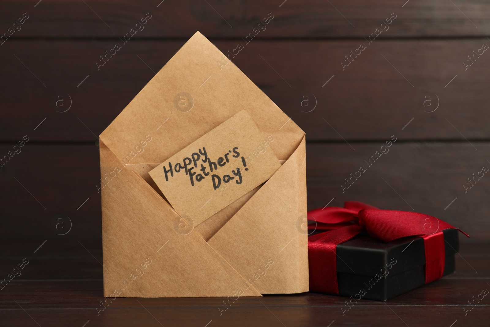 Photo of Card with phrase Happy Father's Day in envelope and gift box on wooden table, closeup