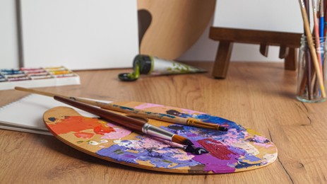 Photo of Artist's palette with mixed paints and brushes on wooden table