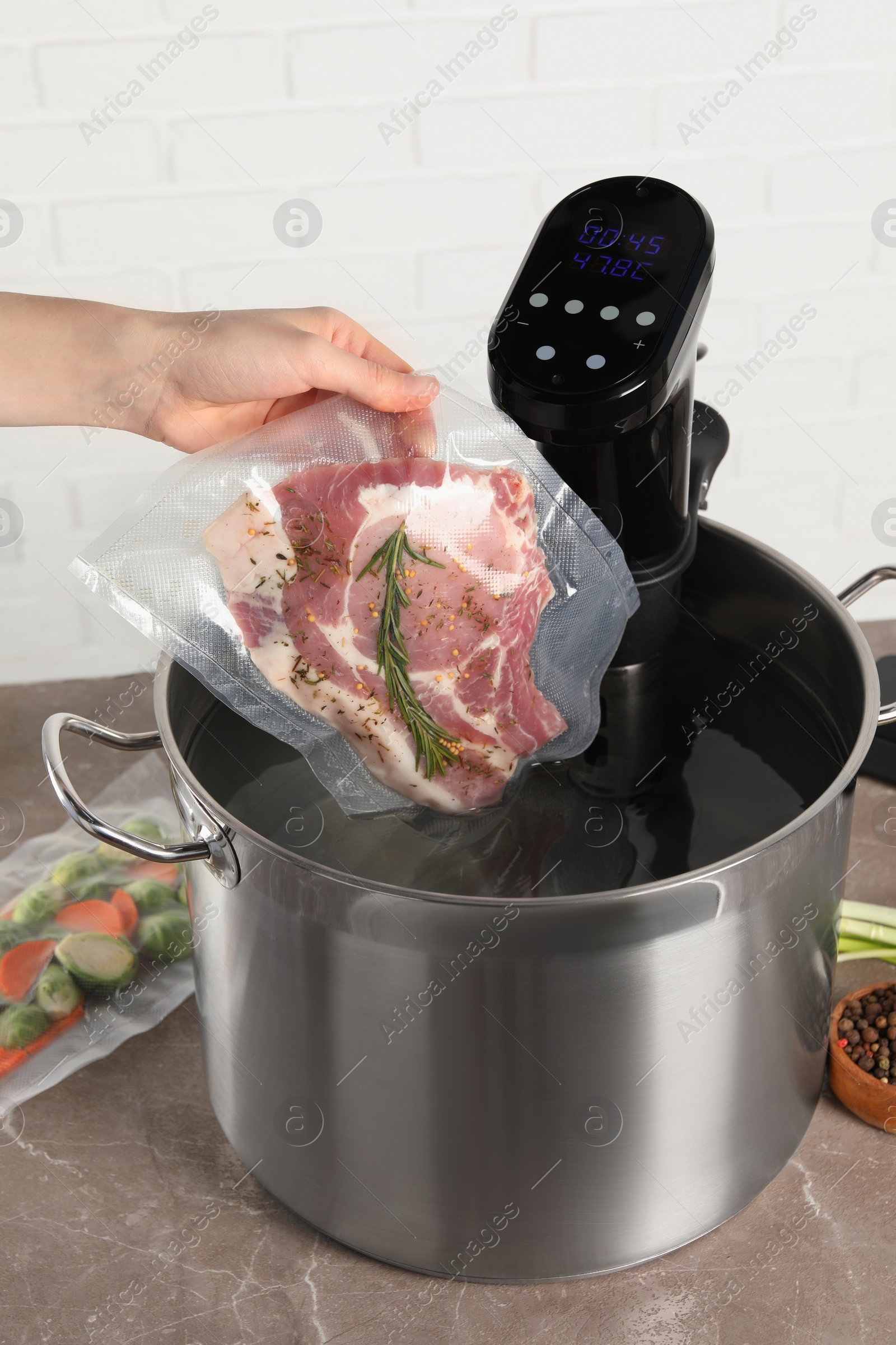 Photo of Woman putting vacuum packed meat into pot with sous vide cooker, closeup. Thermal immersion circulator