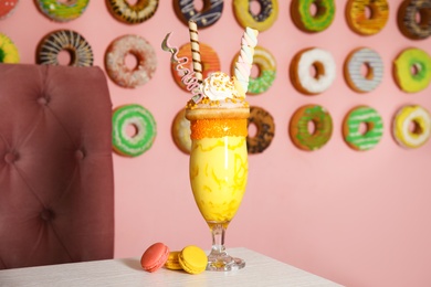 Photo of Glass of tasty milk shake with sweets on table indoors