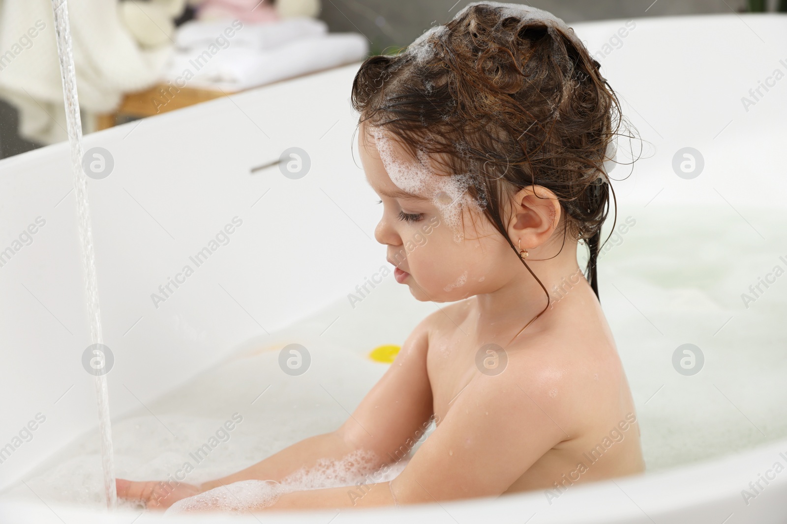 Photo of Cute little girl washing hair with shampoo in bathroom