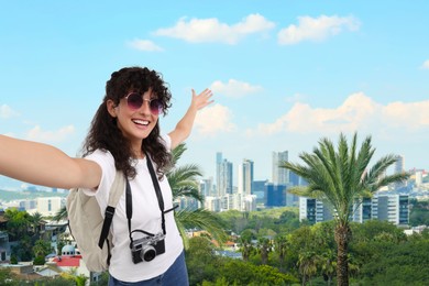 Image of Beautiful woman in sunglasses with camera taking selfie against cityscape