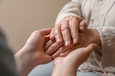 Woman holding hands with her mother on beige background, closeup
